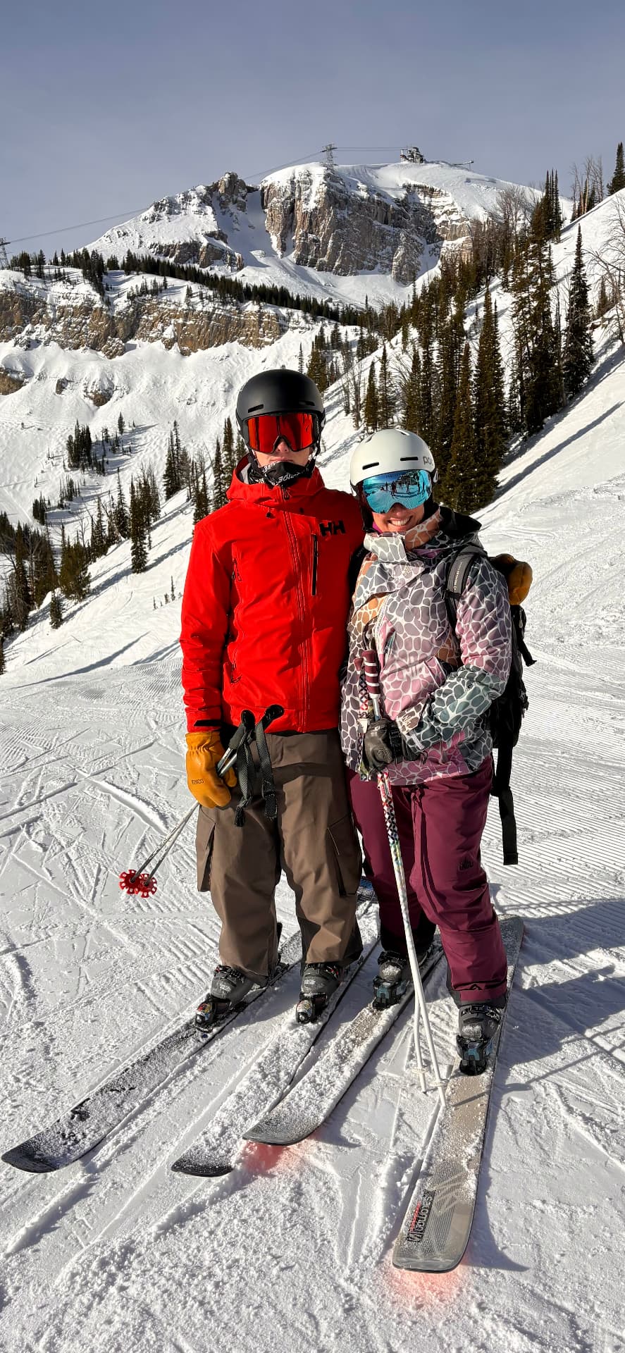 Canyon posing with a skiing partner on a groomed run with a mountain peak behind