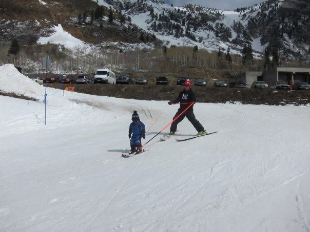 Canyon as a young child learning to ski with training reins held by an adult