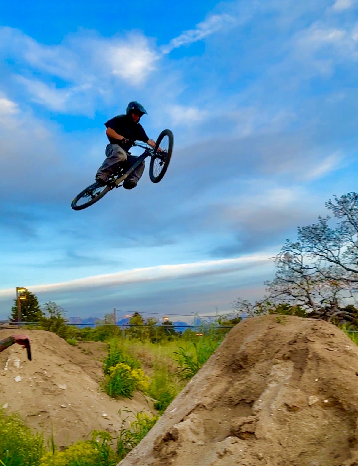 Canyon airborne on his mountain bike over a dirt jump, blue sky behind